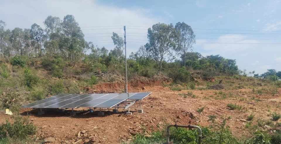 Roadside view of a hillside solar array at Arakanakere with a borewell pipe in the foreground