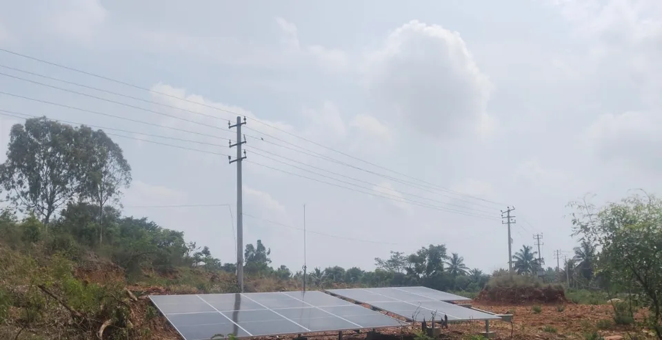 Wide view of two ground-mounted solar arrays set in open scrubland at Arakanakere, Karnataka
