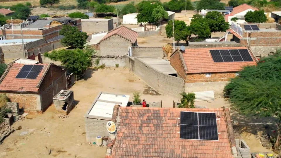 Aerial view of a village of brick houses with tiled roofs, solar panels mounted on several of them.