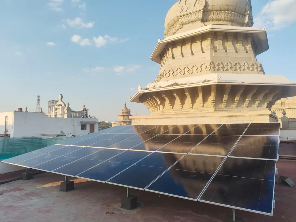 A rooftop solar array in low golden light, set beside one of the building’s stone domes and kept below the parapet line.