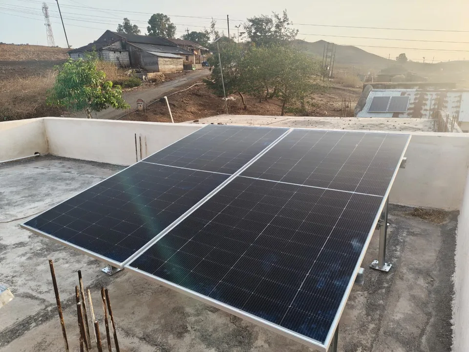 A solar array on a hillside above a village, with terraced fields and scattered houses below it.